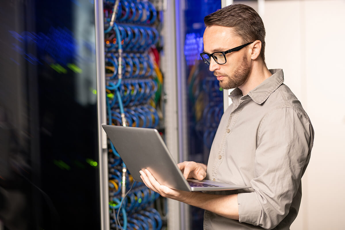 Cyber security expert standing next to server racks on their laptop.